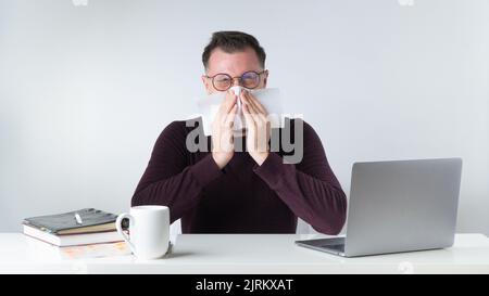 Un uomo starnutisce o soffia il naso sul posto di lavoro in ufficio Foto Stock