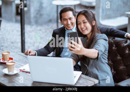 una coppia di lavoro che scatta una foto di se stessa utilizzando lo smartphone Foto Stock
