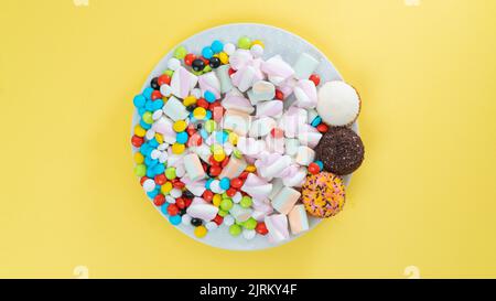 Dolci colorati, marshmallow, torte, dolci e dolci su sfondo giallo brillante Foto Stock