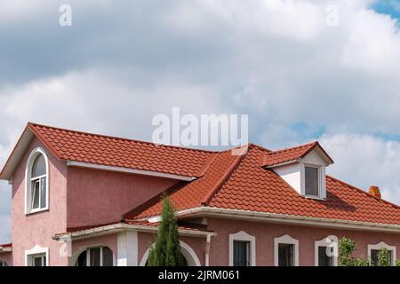 Casa con tetto in mattonelle di metallo rosso marrone chiaro, copertura in metallo scandole contro il cielo blu. Foto Stock