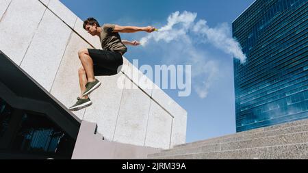 Corridore libero che salta sopra un ostacolo con granate di fumo. Il giovane sportivo che fa parkour stunt all'aperto in città. Foto Stock