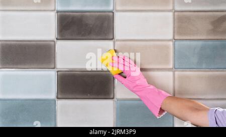 La mano di una donna con guanti di gomma lava le piastrelle con una spugna Foto Stock