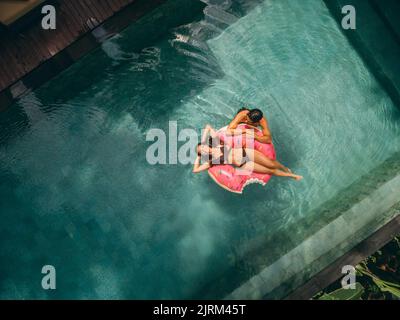 Vista aerea di una giovane donna e di una donna che si rilassano sull'anello gonfiabile nella piscina del resort. Coppia godendo le vacanze in un resort di lusso. Foto Stock