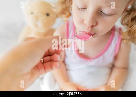 Il bambino beve sciroppo da un cucchiaio dosatore. Foto Stock