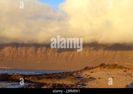 Vista sul Risco de Famara dalla spiaggia di San Juan durante il tramonto Foto Stock