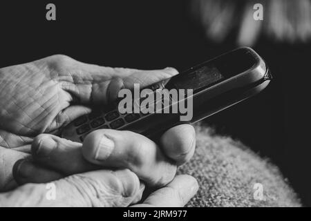 le mani della donna vecchia tengono il telefono a pulsante a casa, pensionato con telefono Foto Stock