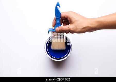 mano che tiene una spazzola messa in una lattina di vernice blu Foto Stock