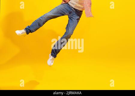 Immagine ritagliata delle gambe maschili in jeans e sneakers bianche isolate su sfondo giallo studio. Incertezza Foto Stock