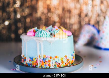 Torta di compleanno colorata con spolverini e berretti di festa sullo sfondo scintillante tinsel d'oro. Festa di compleanno, festa. Messa a fuoco selettiva, Foto Stock