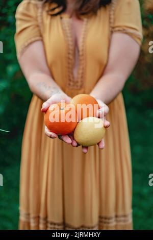 Un primo piano verticale di una donna che tiene il limone e le arance dal suo giardino di casa. Concetto di alimentazione sana. Foto Stock