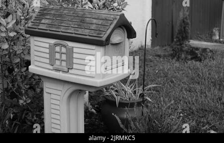 Un primo piano in scala di grigi di una casa di uccello di legno nel giardino Foto Stock
