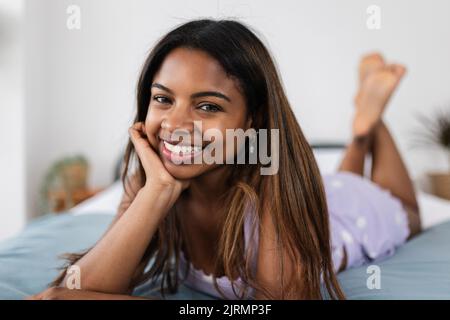 Giovane donna latina sorridente alla macchina fotografica mentre sdraiata a letto a casa Foto Stock