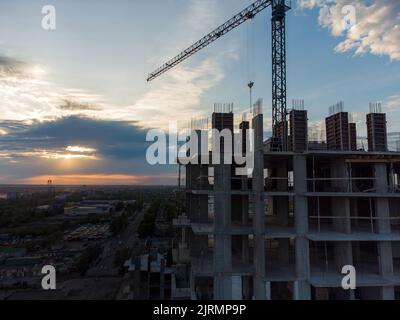 Cantiere con gru sullo sfondo del cielo serale. Gru girevoli a torretta che lavorano al tramonto a sera, edifici sotto Foto Stock