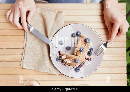 Donna che mangia frittelle tradizionali con mirtilli freschi e sciroppo di agave su un piatto. Colazione all'aperto. Foto Stock