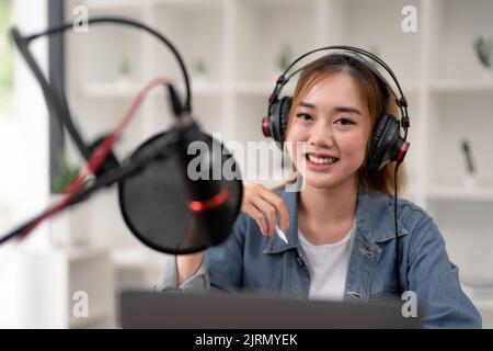 Una giovane donna asiatica effettua una registrazione audio podcast a casa. Foto Stock