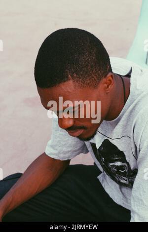 Un colpo verticale di un nigeriano in una camicia grigia seduta fuori Foto Stock