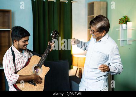 Concentratevi sul vecchio, padre felice con figlio che balla suonando la chitarra a casa - concetto di stile di vita di pensionamento per il tempo libero, legame familiare e libertà Foto Stock