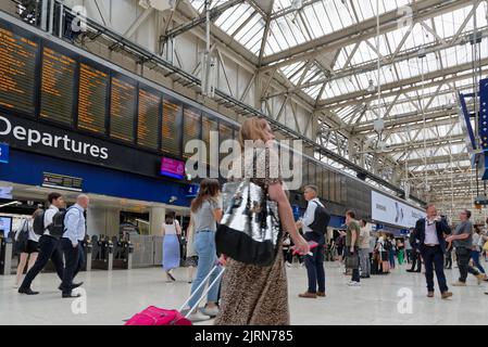 Vista dall'angolo basso dell'atrio della stazione della linea principale di Waterloo con i passeggeri in attesa che guardano il bordo di partenza, Londra, Inghilterra, Regno Unito Foto Stock