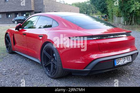 Rheine, NRW, Germania - Agosto 24 2022 Una Porsche Taycan rossa parcheggiata su ghiaia. Si tratta di una berlina elettrica e della prima serie di Porsche elettriche ca Foto Stock