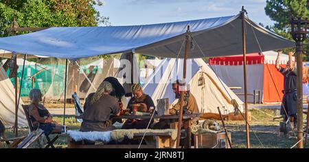 Gifhorn, Germania, 12 agosto 2022: Le persone in costume medievale consumanno un pasto insieme sotto un baldacchino al festival medievale Foto Stock