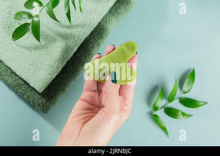 Massaggio mano femminile gua sha raschietto per il viso di pietra verde giada Foto Stock