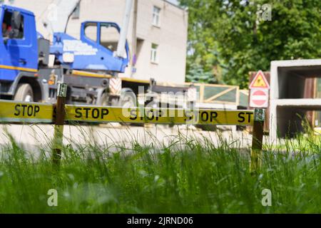 Recinzione in cantiere con nastro giallo con segnale di stop. Sullo sfondo, un'immagine sfocata di un edificio, di strutture edili e di una gru per autocarri. Foto Stock