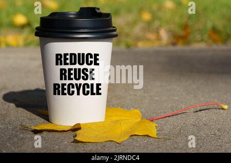 Su una foglia di acero giallo c'è una tazza di caffè su cui è scritto - ridurre, riutilizzare, riciclare. Concetto industriale. Foto Stock