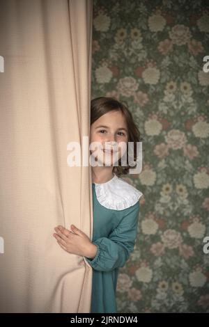 una ragazza carina sbircia fuori da dietro le tende. hide-and-seek Foto Stock