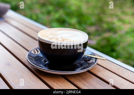 cappuccino o caffè latte in tazza nera sul tavolo di legno all'esterno Foto Stock