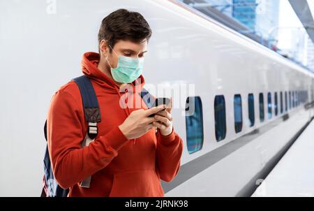 uomo in maschera con smartphone in treno Foto Stock