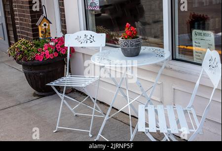 Posti a sedere all'aperto sul marciapiede con tavolo da patio e due sedie con graziosi fiori in vaso sulla strada principale di St Croix Falls, Wisconsin, Stati Uniti. Foto Stock