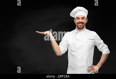 buon cuoco maschio sorridente che tiene qualcosa a portata di mano Foto Stock