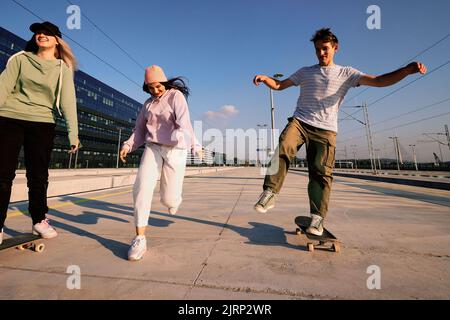 Tre giovani eccitati trascorrono del tempo nell'esterno urbano. Sono in corsa e skateboard. Foto Stock