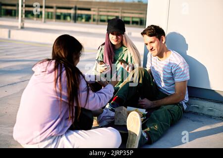 Un piccolo gruppo di adolescenti seduti all'aperto all'esterno della città e appesi ai social media. Adolescenti che provano le app sui loro telefoni. Foto Stock