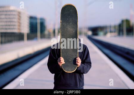 Un ragazzo adolescente è in piedi alla stazione ferroviaria e in possesso di uno skateboard. Foto Stock