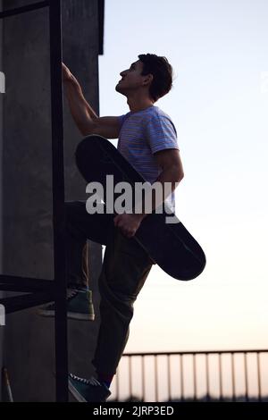 La silhouette di un adolescente ribelle sale le scale su un edificio con uno skateboard in mano. Foto Stock