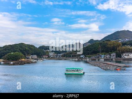 kyushu, giappone - Dicembre 09 2021: Barca da diporto che naviga lungo la costa del Kujukushima Pearl Sea Resort circondato da montagne e zattera di bambù Foto Stock