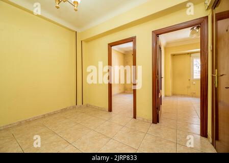 Soggiorno vuoto con pavimenti in gres crema, pareti gialle tenui e legno rossiccio alle porte Foto Stock