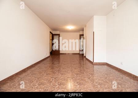 camera vuota con pavimento in gres rossastro, base abbinata, pareti bianche e falegnameria di legno scuro alle porte Foto Stock