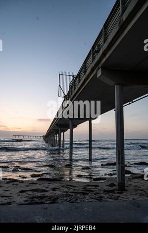Un primo piano di un ponte con onde di mare che si schiantano sulla costa al tramonto Foto Stock
