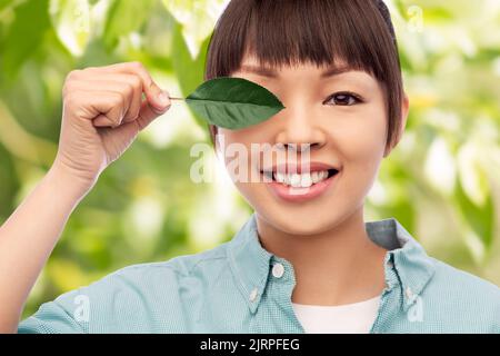 donna asiatica sorridente che tiene verde foglia Foto Stock