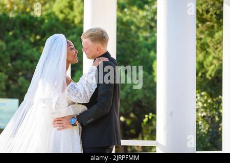 Sposi novelli misti-razziali in una passeggiata abbracciando e amorevolmente guardare l'un l'altro Foto Stock