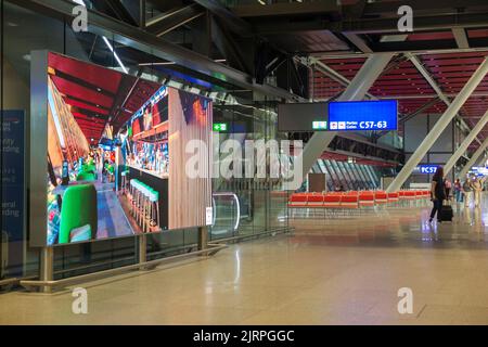 Atrio e grande schermo LCD pubblicitario che mostra immagini in continuo movimento all'interno della nuova sala partenze / architettura moderna modernizzata della sala partenze / sale partenze a Ginevra / Geneve Aeroporto 'Cointrin' Svizzera. (131) Foto Stock
