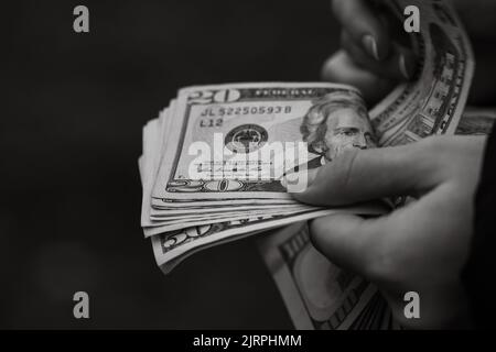 Un colpo in scala di grigi di una persona che tiene le banconote del dollaro degli Stati Uniti nelle mani Foto Stock