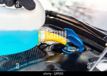 Dettaglio primo piano della mano del conducente o meccanico nei guanti che versano liquido antigelo blu per lavaggio parabrezza invernale auto con annaffiatoio bootle Foto Stock