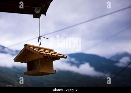 Birdhouse marrone legno sospeso da un tetto con montagne e cielo d'inverno sullo sfondo. Sfondo con spazio per la copia. Idea di ecologia del giardino. Foto Stock