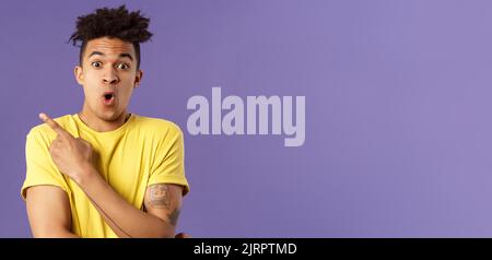 Ritratto di sorpreso, eccitato giovane uomo mostrando cool nuova cosa, punta in alto a sinistra angolo, gasping, labbra pieghevoli, stare fotocamera impressionato dire wow Foto Stock