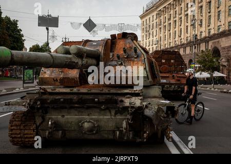 Kiev, Ucraina. 23rd ago, 2022. Un uomo con una bicicletta osserva il relitto del carro armato russo distrutto a Kiev. Dedicato alla prossima Giornata dell'Indipendenza dell'Ucraina, e quasi 6 mesi dopo l'invasione su larga scala dell'Ucraina il 24 febbraio, la capitale del paese Kyiv ha tenuto una mostra sulla strada principale di Khreschaytk Street che mostra le attrezzature militari distrutte, Carri armati e armi dalle forze armate della Federazione Russa (AFRF). Come la piena invasione russa dell'Ucraina iniziato il 24 febbraio, la guerra ha ucciso numerosi civili e soldati, quasi 9000 militari ucraini Foto Stock