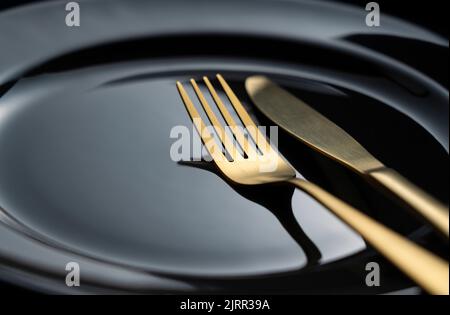 Un coltello dorato e una forchetta su un piatto nero. Belle posate d'oro. Primo piano. Foto Stock