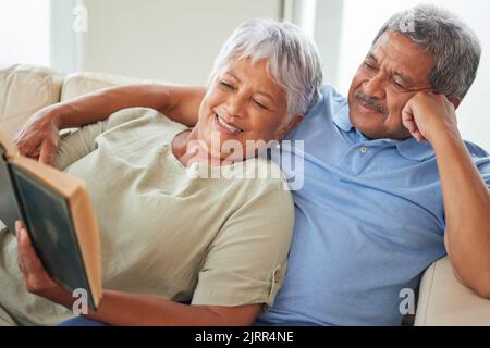 Rilassatevi, coppia felice e anziana leggendo un libro insieme a casa mentre vi rilassate e sorridenti su un divano. Gli amanti maturi o vecchi imparano e riposano mentre Foto Stock